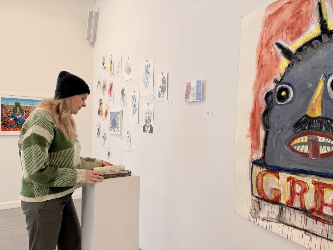 Kuratorin Anne-Marie Stöhr blättert in einer Arbeit von Peter Mann, der die Seiten von Arthur Koestlers „Abschaum der Erde“ bemalt mit Szenen aus der US-amerikanischen Politik.