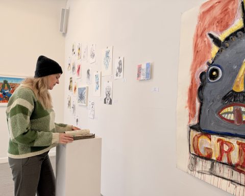 Kuratorin Anne-Marie Stöhr blättert in einer Arbeit von Peter Mann, der die Seiten von Arthur Koestlers „Abschaum der Erde“ bemalt mit Szenen aus der US-amerikanischen Politik.